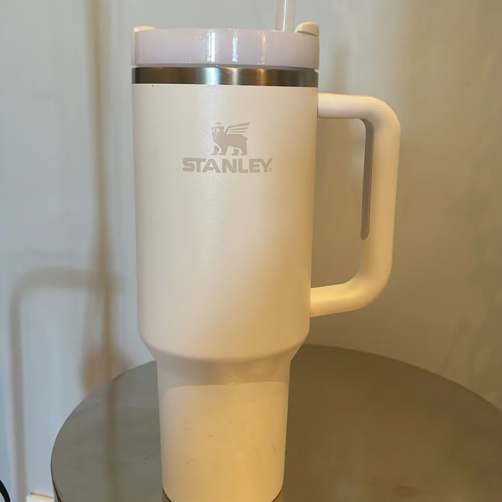 Säljer en stilren vit termosmugg från Stanley med handtag och sugrör. Perfekt för att hålla drycker varma eller kalla under dagen. Muggen har en kapacitet på 40 oz/1,1 L och är idealisk för både vardag och äventyr.. Muu.
