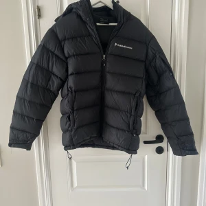 Svart dunjacka från Peak Performance - Säljer en svart dunjacka från Peak Performance. Jackan har en dragkedja framtill och är långärmad med en skön huva. Perfekt för kyliga dagar och håller dig varm och bekväm. 🖤