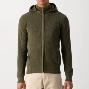 Olivgrön cardigan - Säljer en olivgrön ribbad cardigan med dragkedja och huva. Den har långa ärmar och praktiska fickor med dragkedja framtill. Perfekt för en avslappnad stil. DET ÄR STORLEK M HELT NY ALDRIG ANVÄND PRISLAPP PÅ.