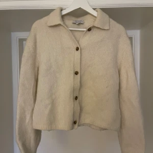 Vit stickad kofta från & Other Stories - Säljer en vit stickad kofta från & Other Stories. Koftan har långa ärmar och knäpps med knappar framtill. Den är använd och därav nopprig på insidan av armarna (se bild). Storlek M. Den är tillverkad i alpacka, polyamid och ull. 