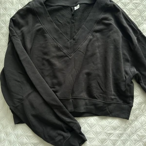 Mörkgrå v-ringad tröja - Säljer en stilren mörkgrå tröja med v-ringning. Tröjan har långa ärmar och ribbade muddar vid ärmslut och nederkant. Perfekt för en avslappnad look. Supersnyggt att ha den lite över axeln med ett par snygga byxor🦋