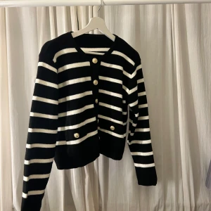 Svart och vit randig kofta med knappar - Snygg svart och vit randig kofta med guldknappar framtill. Använd 1 gång, kommer inte till någon användning.