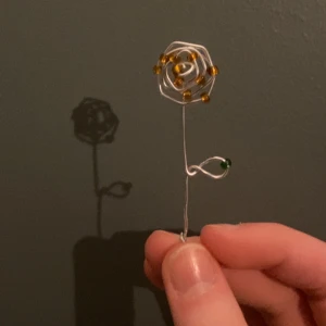 Ros  - Blomma formad av ståltråd och dekorerad med små orange och gröna pärlor. Blomman kan hängas i en tunn silverkedja och ger en konstnärlig touch till din stil. Jag gör smycken med pärlor så säg bara till om det finns önskemål! 
