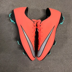 Nike mercurial vapor - Snygga röda fotbollsskor från Nike med svarta och turkosa detaljer. Skorna har en slimmad passform och är designade för att ge bra grepp på planen. Perfekta för fotbollsträning och matcher.