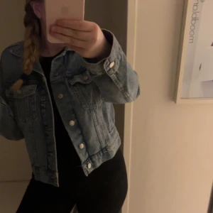 Blå jeansjacka - Säljer en klassisk blå jeansjacka med knappar framtill. Jackan har en normal passform och långa ärmar. Perfekt för vår och sommar! I jätte bra skick då den aldrig är använd!