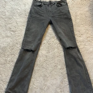 Grå jeans med slitna detaljer - Säljer ett par grå jeans från Gina Tricot med slitna knän och rå kant upptill. De har en dragkedja samt fem fickor. Jag har själv designat jeansen, använda under 10 gånger och är i bra skick. Original priset ligger på 500kr.