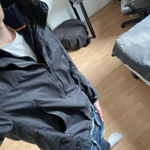 Svart vindjacka från Colmar - Säljer en stilren svart vindjacka från Colmar. Jackan har en dragkedja framtill och en praktisk huva. Perfekt för blåsiga dagar och har en normal passform. En diskret logga finns på ärmen.