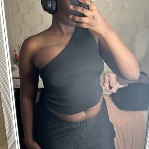 Svart ribbad oneshoulder topp - Snygg svart oneshoulder topp med ribbad textur. Perfekt för en stilren look. Toppen är croppad och ger en modern touch till din outfit 🖤