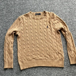 Beige kabelstickad tröja från Ralph Lauren - Säljer en klassisk beige kabelstickad tröja från Ralph Lauren. Tröjan har en broderad logotyp på bröstet och är tillverkad i 100% bomull. Perfekt för en stilren och bekväm look. Skick:9/10 inga defekter 