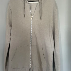 Grå hoodie från The Black Label Collection - Säljer en stilren grå hoodie från The Black Label Collection. Den har en dragkedja framtill och praktiska fickor. Perfekt för en avslappnad look.