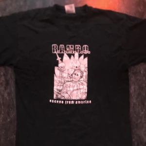 Svart t-shirt med Rambo-tryck - Cool svart t-shirt med ett unikt Rambo-tryck i vitt. Perfekt för filmälskare som vill ha en avslappnad stil. T-shirten har korta ärmar och en normal passform.