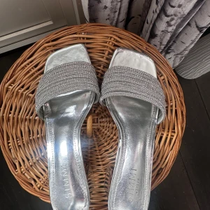 Silvriga sandaler med klack - Snygga silvriga sandaler från Simmi med en glittrig rem över foten. De har en elegant klack och öppen tå, perfekt för festliga tillfällen. Sandalerna har en stilren design som ger en lyxig känsla.