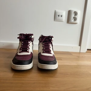 Nike sneakers i vinrött och svart - Snygga Nike sneakers i vinrött, svart och vitt. Skorna har en klassisk design med snörning och rund tå. Perfekta för en stilren look.