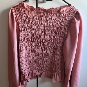 Rosa blus från Sisters Point - Säljer en söt rosa blus från Sisters Point med smockdetaljer och volangkant. Blusen har långa ärmar och en bekväm passform. Perfekt för en stilren look!🌸  Storlek L men passar som S/M använt ett handtag av gånger, den är i jättebra skick. Säljer för att den är för lite. 