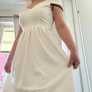 Vit klänning med offshoulder-design passar perfekt student eller fest kläder  - Säljer en elegant vit klänning med offshoulder-design och v-ringad hals. Klänningen har en kort längd och är perfekt för sommarens tillfällen. Den har en stilren och klassisk look som passar till många olika stilar.