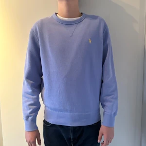 Ljusblå tröja från Ralph Lauren - Säljer en stilren ljusblå tröja från Ralph Lauren med rund hals. Perfekt för en avslappnad och snygg look. Tröjan har långa ärmar och ribbade muddar. Passar till våren och sommaren