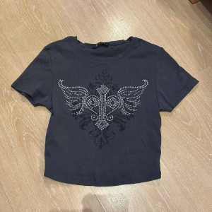 Svart kortärmad t-shirt med strassdetaljer - Y2K topp. Snygg svart t-shirt med korta ärmar och ett coolt strassmönster framtill. Perfekt för att ge din outfit lite extra bling! 💎