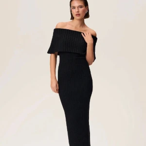 Svart ribbad adoore offshoulder klänning - Snygg svart ribbad klänning med offshoulder-design. Perfekt för en stilren look. Klänningen är lång och har en tight passform som framhäver figuren.
