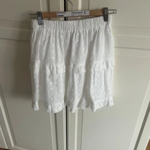 Vit kjol från Elenza - Säljer en söt vit kjol från Elenza med broderade blommor och volanger. Kjolen har en elastisk midja för en bekväm passform. Passar S-M. Aldrig använd nypris 600 kr❤️