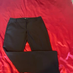 Lågmidjade kostymbyxor från bikbok - Eleganta svarta kostymbyxor med en klassisk passform. Byxorna har en rak stil och är perfekta för en stilren look. De har diskreta fickor och en knappstängning framtill. Byxorna är i stilen ”Vera”.❤️