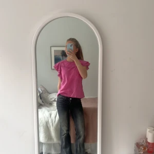 Rosa blus med volangdetaljer - Säljer en söt rosa blus med volangdetaljer på ärmarna. Blusen har korta ärmar och dekorativa spetsdetaljer längs halsringningen och ärmarna. Perfekt för en somrig look! Inga skador🩷🩷