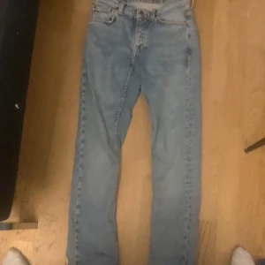 Blå jeans från Nudie Jeans - Säljer ett par klassiska blå jeans från Nudie Jeans. De har en normal passform och är tillverkade i denim. Jeansen har en traditionell femficksdesign och en knappgylf. Perfekta för en avslappnad stil.