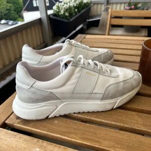 Axel Arigato - Genesis vintage runner - Säljer ett par stilrena vita sneakers från Axel Arigato med grå mockadetaljer och vit sula. Skornas nypris är 2700 kr. Observera små ”fläckar” fram på ena skon, därav det låga priset. Har själv inte försökt ta bort fläckarna med mer än ett blött papper. Storlek 46 men passar bättre till de som har storlek 44-45. Jag har själv storlek 44.5 i vanliga fall. 