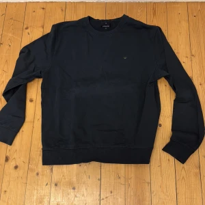 Svart sweatshirt från Junk de Luxe - Säljer en svart sweatshirt från Junk de Luxe i ekologisk bomull. Tröjan har rund halsringning, långa ärmar och en liten broderad krona på bröstet. Enkel och stilren modell som passar till det mesta.