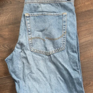 Ljusblå jeans från Jack & Jones - Säljer ett par klassiska ljusblå jeans från Jack & Jones med femficksdesign och kontrastsömmar. Jeansen har normal passform och raka ben, perfekta till vardags. Tidlös modell med snygga detaljer på bakfickan.