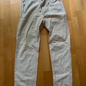 Beige linnebyxor med normal passform - Säljer ett par ljusbeige linnebyxor från kappahl med raka ben och klassisk design. Byxorna har sidfickor, knapp och dragkedja framtill samt en bakficka med knapp. Perfekta för varmare dagar och enkel stil.