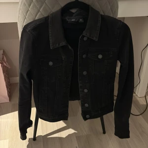Svart jeansjacka från Vero Moda - Säljer en svart jeansjacka från Vero Moda i storlek XS. Klassisk modell med knappar framtill, två bröstfickor med lock och knapp samt krage. Perfekt att slänga över en hoodie eller t-shirt! Använd endast 1 gång!💓