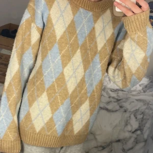 Beige och blå stickad tröja från Lindex - Säljer en stickad tröja från Lindex i barnstorlek 146/152. Tröjan har ett klassiskt argylemönster i beige, ljusblått och vitt, med ribbade muddar och rund hals. Perfekt för en childag hemma.