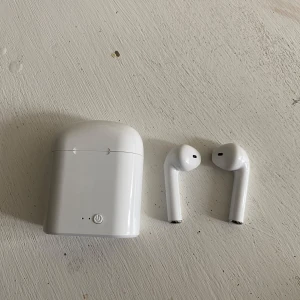 Trådlösa vita hörlurar med laddningsetui - Säljer ett par trådlösa vita hörlurar med tillhörande laddningsetui. Hörlurarna har en stilren och minimalistisk design med rundade kanter och touchknapp på etuiet. Laddas via micro-USB-port på baksidan.