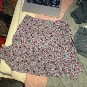 Blommig omlottkjol från FB Sister - Säljer en söt blommig omlottkjol från FB Sister i storlek S. Kjolen har volangdetalj nertill och knyts i midjan. Färgerna går i lila, rosa, blått och vitt. Perfekt för vår och sommar!