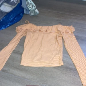 Gul- och vitrandig offshoulder-top från Gina Tricot - Säljer en gul- och vitrandig offshoulder-top från Gina Tricot. Toppen har långa ärmar, volangdetalj längs axeln och är croppad i modellen. Perfekt för dig som gillar unika detaljer och en färgglad stil!