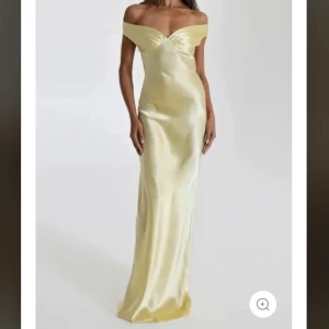 Ljus gul långklänning i satin - Elegant balklänning/långklänning i skimrande ljus gul satin med offshoulder-skärning och lätt v-ringad detalj framtill. Klänningen har figurnära passform och släpper mjukt längs kroppen för en lyxig känsla. Nypris 1148 kr