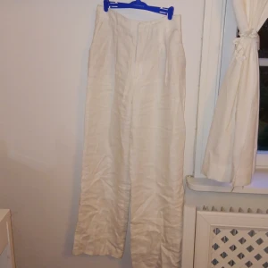 Vita linnebyxor med raka ben - Säljer ett par vita linnebyxor med raka,vida ben. Byxorna har diskreta fickor framtill och stängs med dragkedja. Perfekta för varmare dagar och ger en avslappnad men stilren look.
