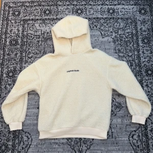 Beige hoodie från Jack & Jones - Mysig vit hoodie från Jack & Jones Originals med broderad text 'Originals Studio' på bröstet. Tröjan är tillverkad i teddy-material Perfekt för kalla dagar när du vill vara varm. 