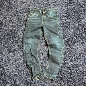 G-Star Raw jeans med slitna detaljer - Säljer ett par mörkblå jeans från G-Star Raw med slitna detaljer och råa benslut. Byxorna har klassisk femficksdesign, gylf med dragkedja och knappar samt stora och dekorativa sömmar på bakfickorna. Hör av er vid minsta fundering🙌