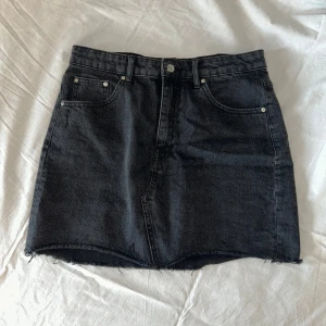 Svart jeanskjol  - Säljer en jättesnygg svart jeanskjol med fransig nederkant från Gina tricot. Kjolen har knapp och dragkedja framtill samt bälteshällor.💗