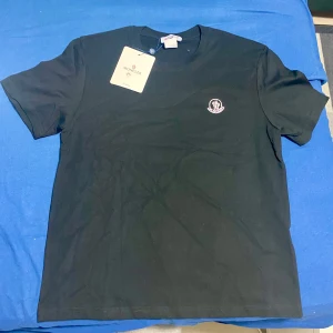 Svart t-shirt från Moncler - Säljer en svart t-shirt från Moncler med klassisk rund hals och Moncler-logga tryckt på bröstet. T-shirten är i mjuk bomull och har en enkel, stilren design som passar perfekt till jeans eller shorts.
