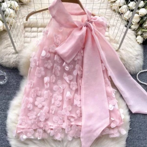 Rosa blommig Blus med stor rosett - Supersöt rosa Blus med 3D-blommor och en stor rosett vid halsen. Blusen  är ärmlös och har en lätt A-linjeformad siluett. Perfekt för speciella tillfällen när du vill känna dig extra fin.
