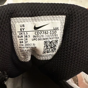 Nike sneakers med röd swoosh och svart-vit design - Säljer ett par Nike sneakers i storlek 38,5 med vit bas, svarta detaljer och röd swoosh. Högt skaft med snörning och svart kardborreband upptill. Klassisk streetstil som passar perfekt till vardagslooken.