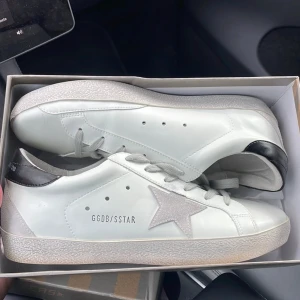 Vita sneakers med silverstjärna från Golden Goose - Säljer ett par vita sneakers från Golden Goose. Skorna har snörning och platt sula. Perfekta för en stilren och trendig look. Skorna är helt fabriksnya och aldrig använda. Lådan medföljer 
