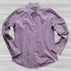 Ralph Lauren - Säljer en klassisk rutig skjorta från Ralph Lauren i rött, blått och vitt. Skjortan har lång ärm, knappar framtill och broderad logga på bröstet. Perfekt för dig som gillar stilrena och tidlösa plagg.