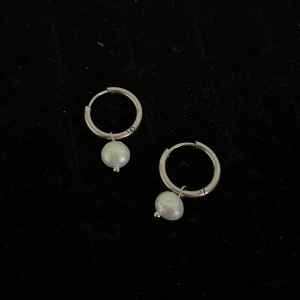 Silverörhängen med pärlor - Säljer ett par stilrena örhängen i silver med hängande vita pärlor. Perfekta för att ge en elegant touch till din look. Enkla ringar med en klassisk pärldetalj.