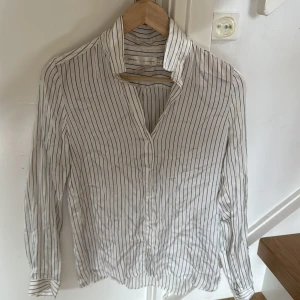 Vit och svart randig skjorta i satin från InWear - Säljer en klassisk vit skjorta med svarta ränder från InWear, modell Leonore Shirt. Skjortan har lång ärm, krage och knäppning framtill. Perfekt för en stilren och tidlös look.