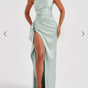 Ljusgrön långklänning i satin med slits - Ljusgrön långklänning i satin från BabyBoo med oneshoulder och slits framtill med en draperad midja. Klänningen har justerbara band i ryggen. Endast använd 1 gång. Sliten är även igensydd (går att sprätta upp utan att lämna markering)
