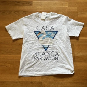 Vit Casablanca t-shirt - Vit t-shirt från Casablanca Tennis Club med tryck av en svan och texten 'Casa Blanca Par Avion' på framsidan. Klassisk passform och rund hals. Perfekt för en stilren och sportig look.
