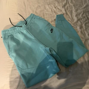 Turkosa mjukisbyxor från Nike - Säljer ett par turkosa mjukisbyxor från Nike med resår och snörning i midjan. Byxorna har två sidofickor och en liten Nike-logga på vänster lår. Perfekta för en avslappnad stil. Nypris 1000. 